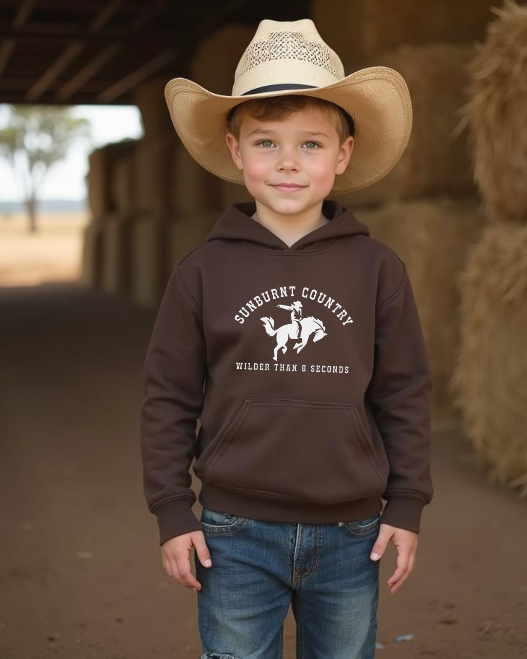 Young boy wearing a Sunburnt Country Clothing Wilder Than 8 Seconds brown kids country hoodie with bucking bronc design