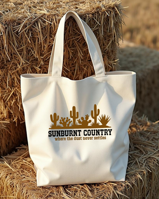 Sunburnt Country Clothing canvas tote bag with 'Sunburnt Country' text and cactus design on hay bales.