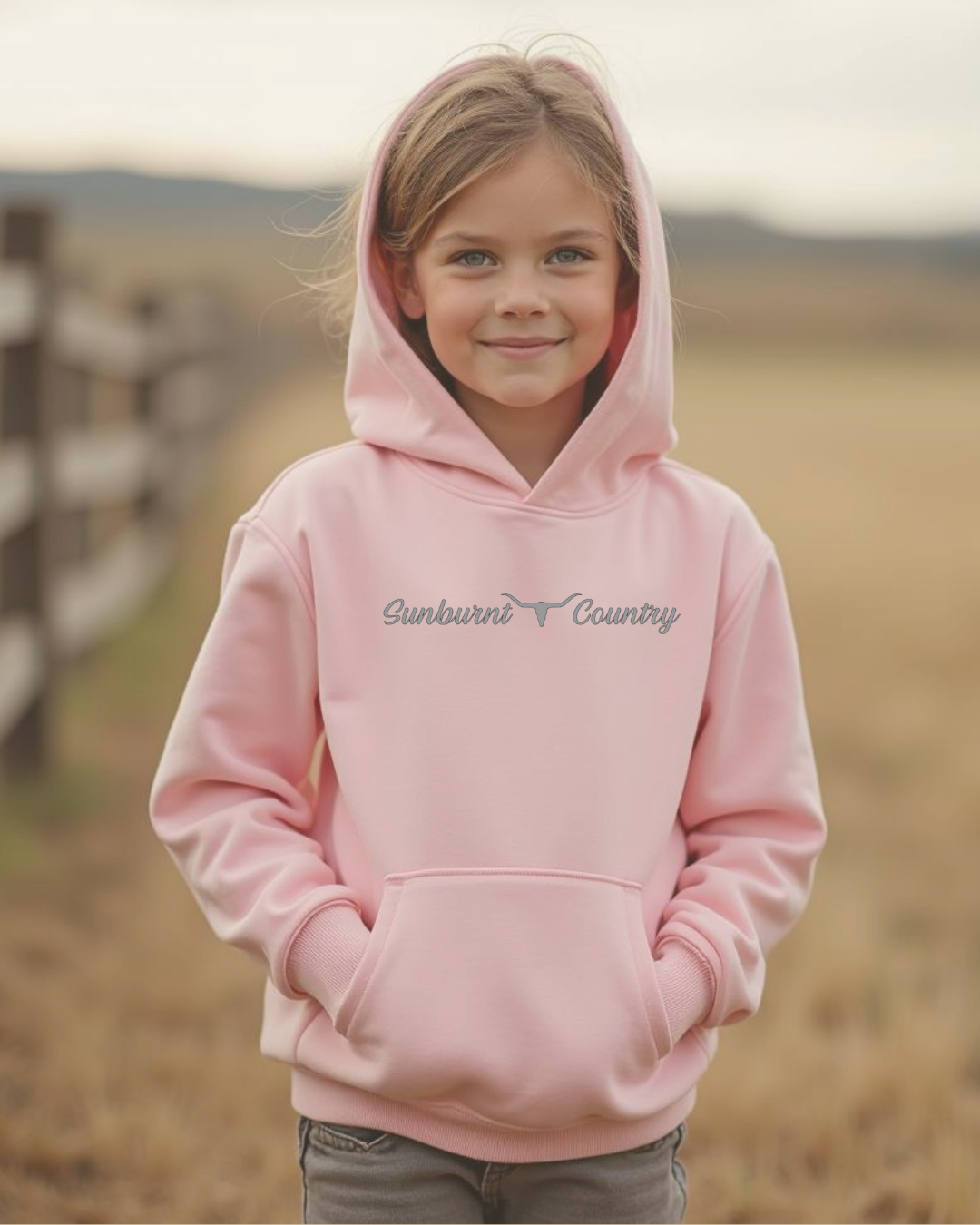 Front of a Young girl wearing a pink coloured girls country western hoodie with small longhorn and text design by Sunburnt Country Clothing, Australian kids country clothing