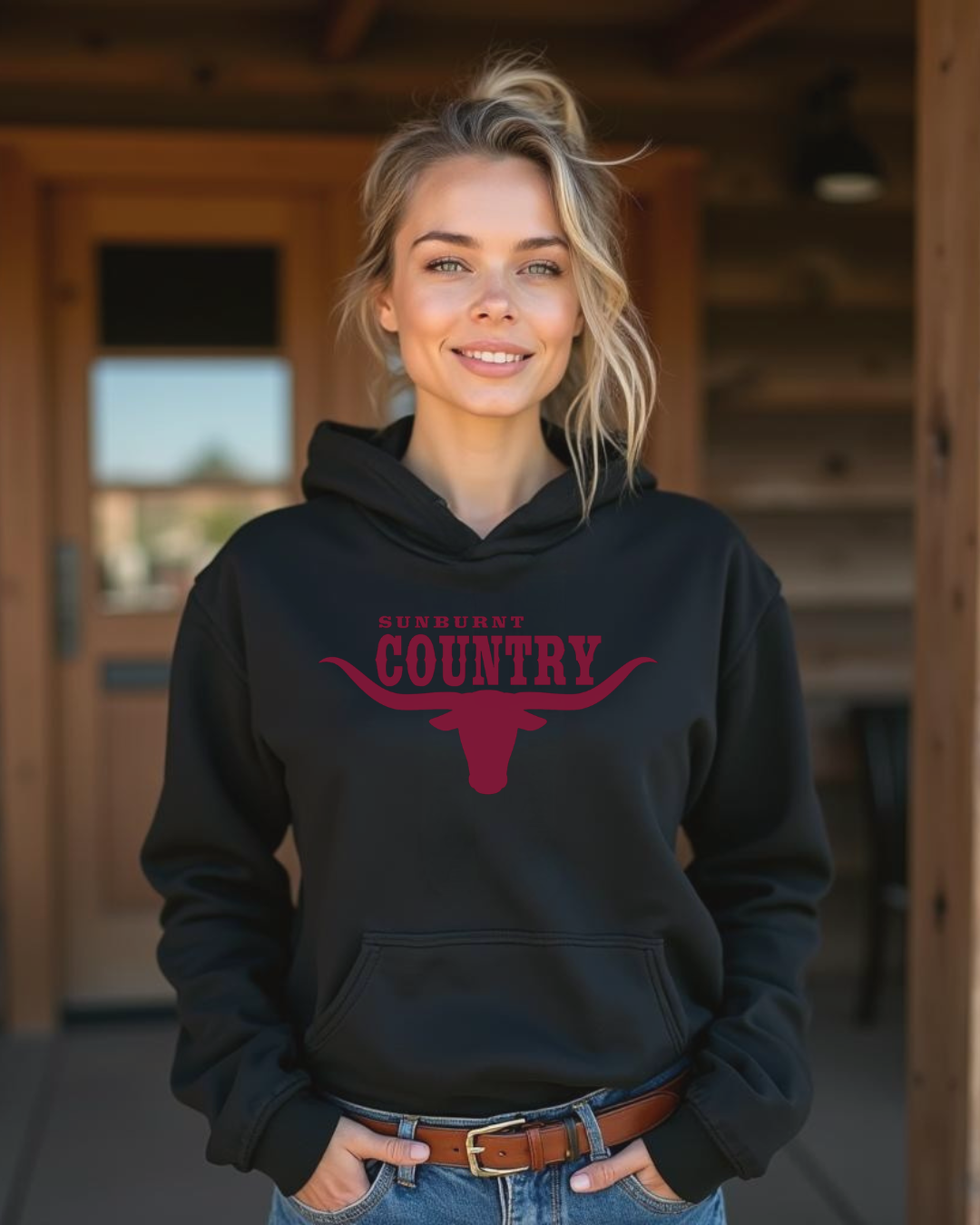 Women wearing a black hoodie with 'Sunburnt Country' text, and a longhorn logo standing in a wooden interior setting.
