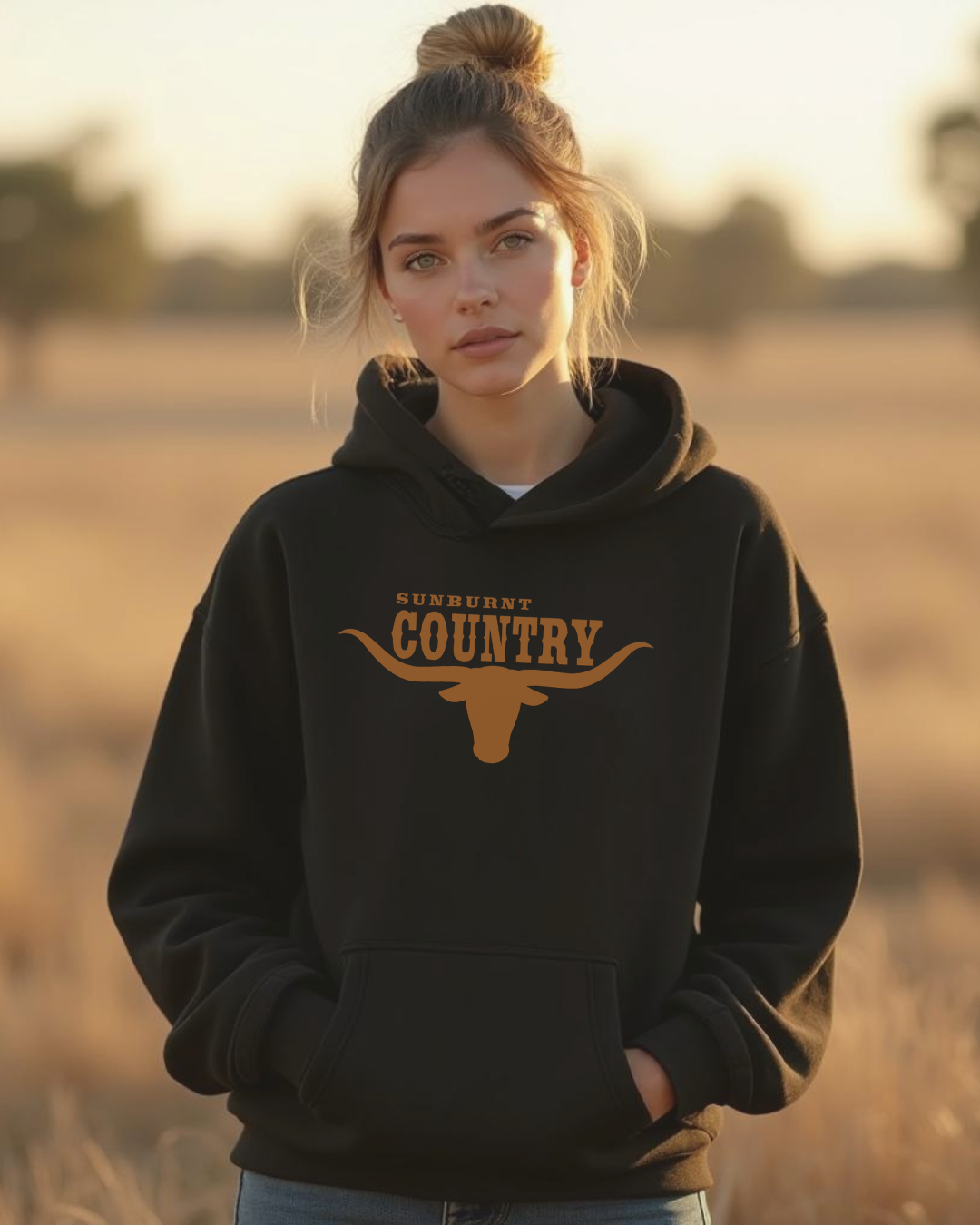 Woman wearing a black hoodie with 'Sunburnt Country' logo with longhorn design in a field