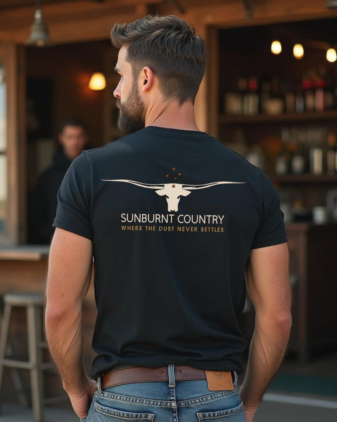 Back of Male model wearing Sunburnt Country Clothing Where the dust never settles longhorn tee in rural setting
